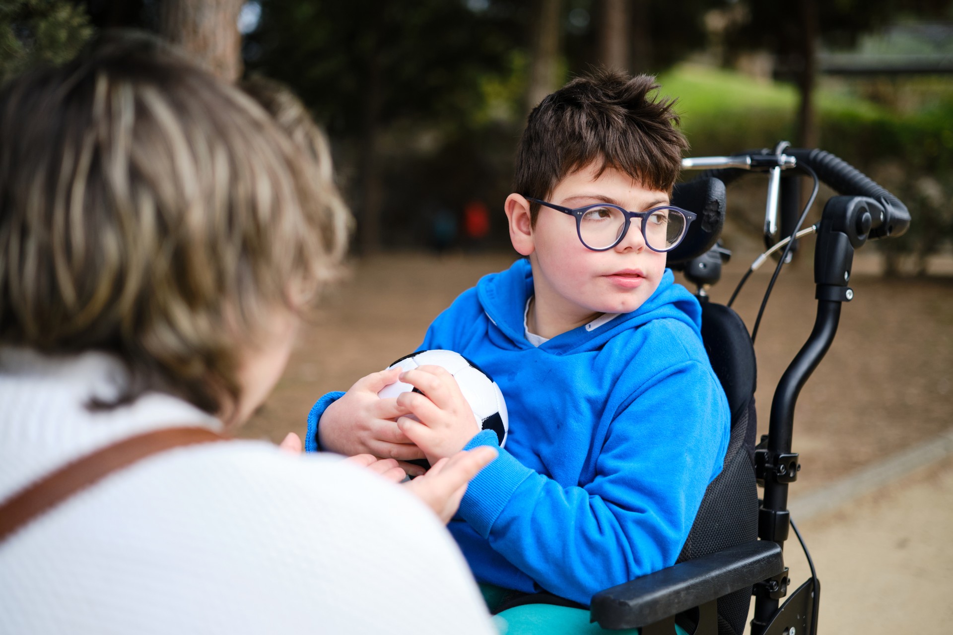 Disabled boy in a wheelchair with a soccer ball while enjoying playing with his mother in the park.