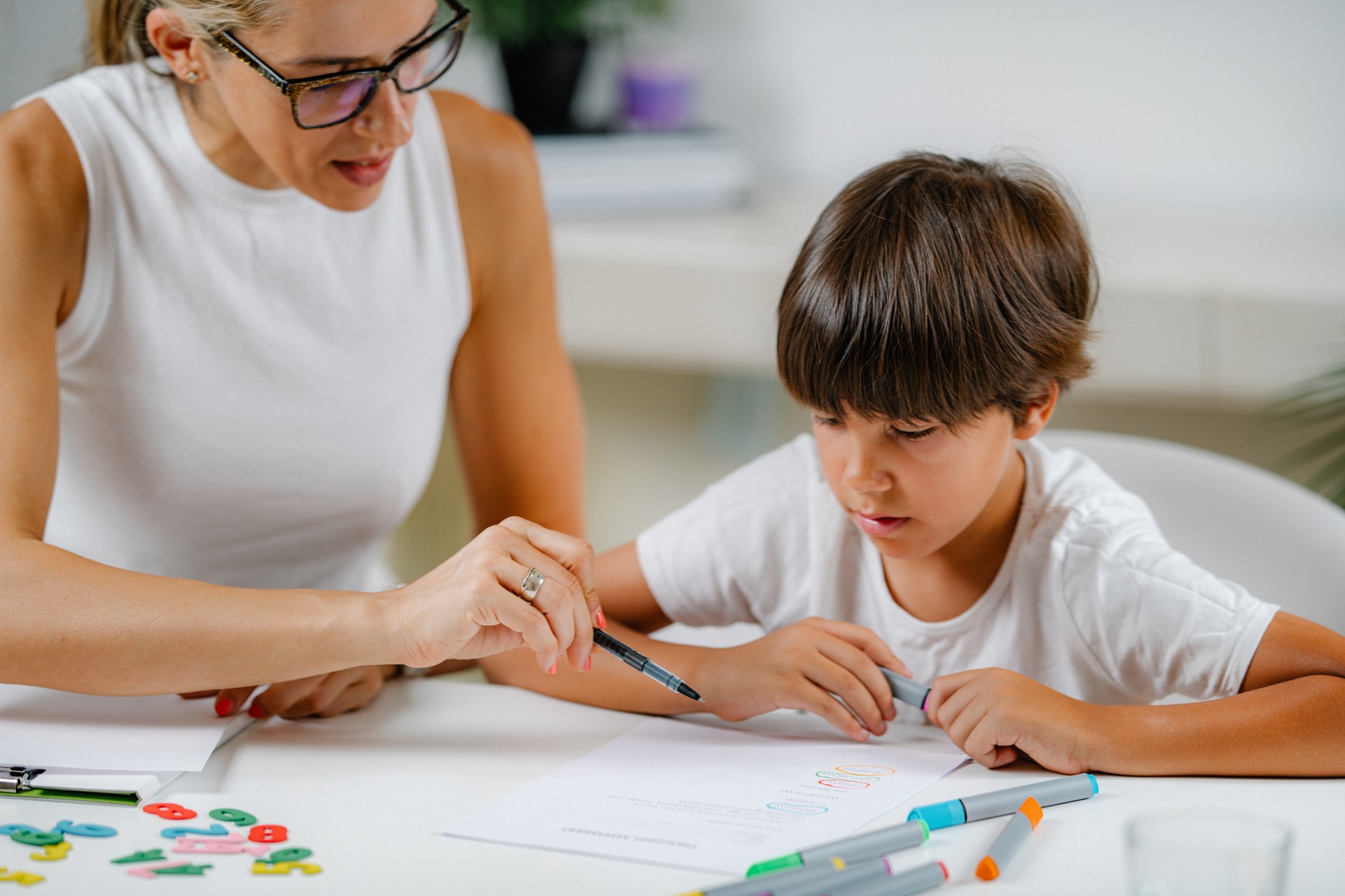 Preschool boy doing school education assessment test. Psychologist asking a questions and preschool boy writing answers.